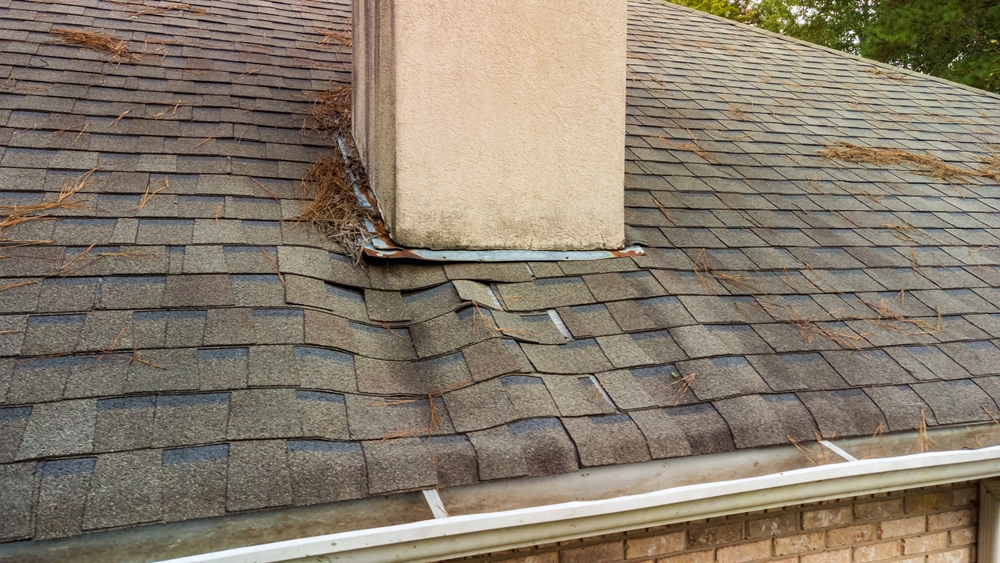 A damaged roof with visible water leaking through cracked and missing shingles.