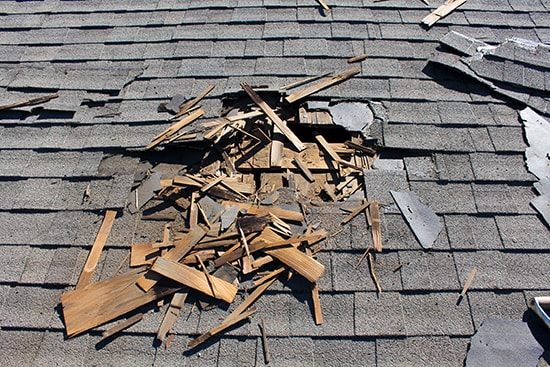 A roof showing wind damage with missing and lifted shingles exposing the underlayment.