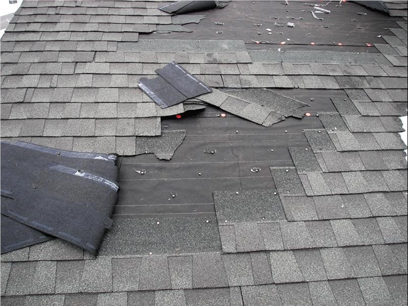 Alt text: A roof showing wind damage with shingles lifted and missing after a storm.